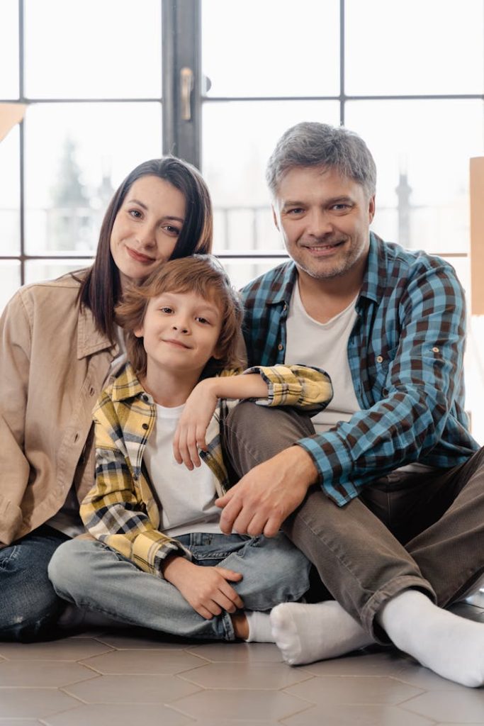man-in-brown-dress-shirt-sitting-beside-woman-in-brown-coat-7415126 A smiling family sitting on the floor of their new home, enjoying a cozy moment.