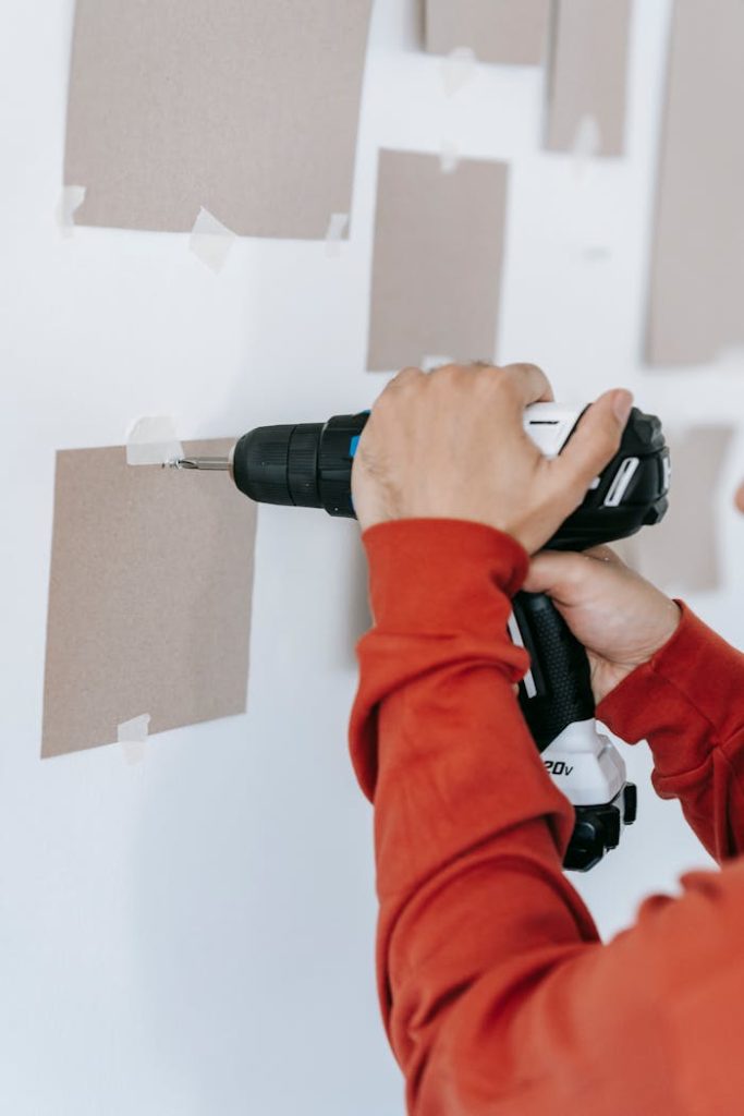 person-drilling-a-hole-on-wall-7218101 Close-up of hands using a drill on wall in home improvement setting.