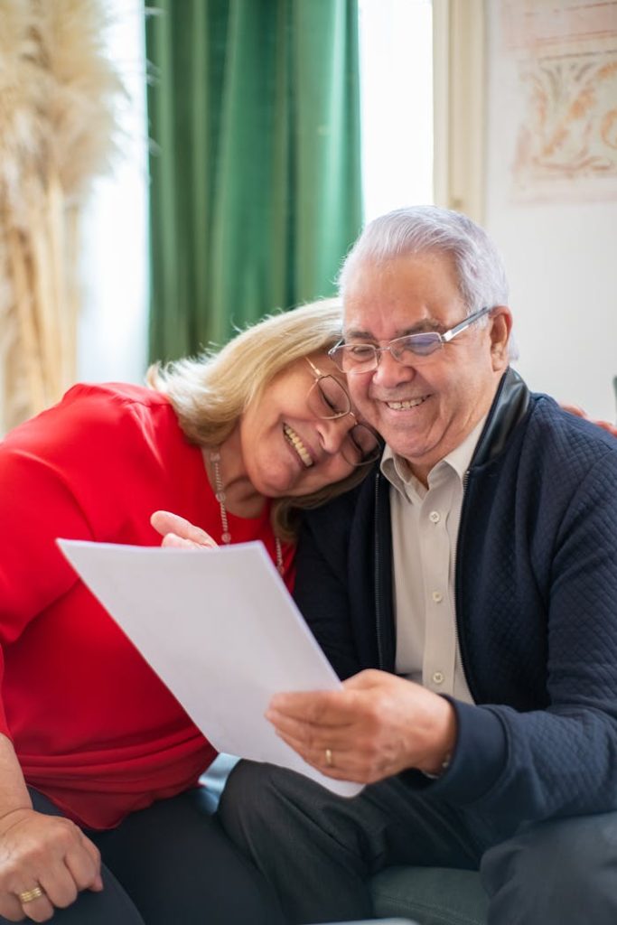 portrait-of-a-romantic-elderly-couple-8439683 Elderly couple smiling together while looking at a document, showcasing love and happiness indoors.